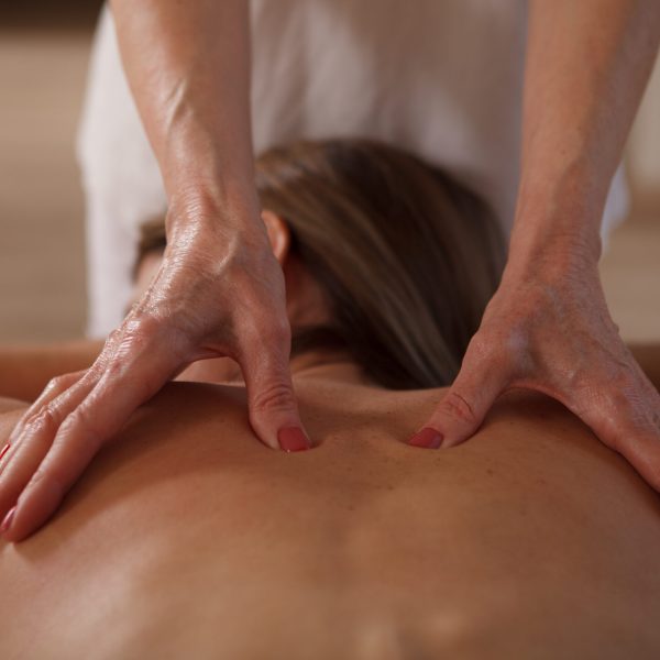 Close up of hands of professional masseuse working at spa, massaging back of female client